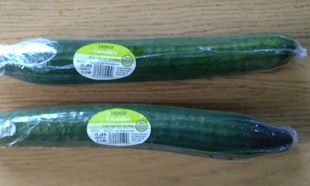 Image of two shrink wrapped cucumbers placed length ways on a wooden background.